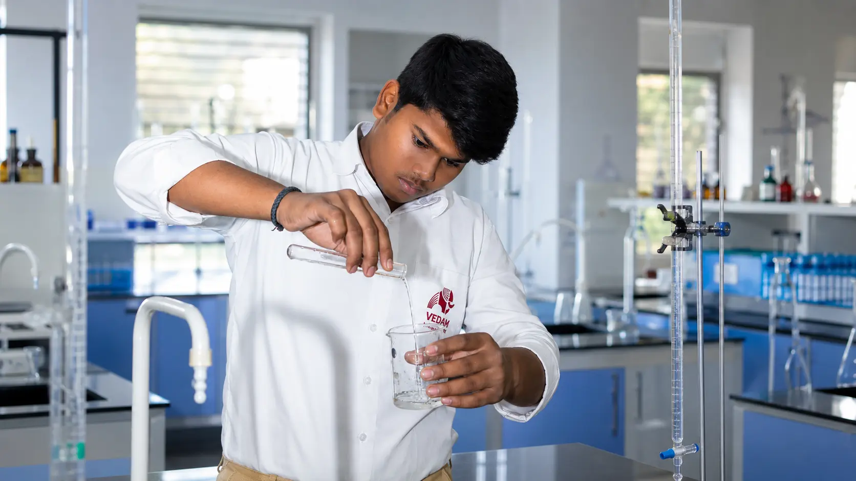 Student carefully pouring a measured sample during a chemistry practical — Sitapur Road campus, VEDAM World School