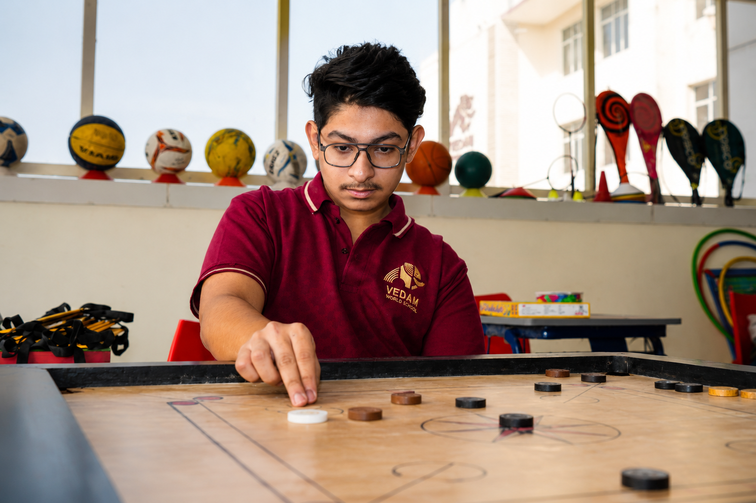 Student playing carrom in the indoor games room — Ayodhya Road campus, VEDAM World School